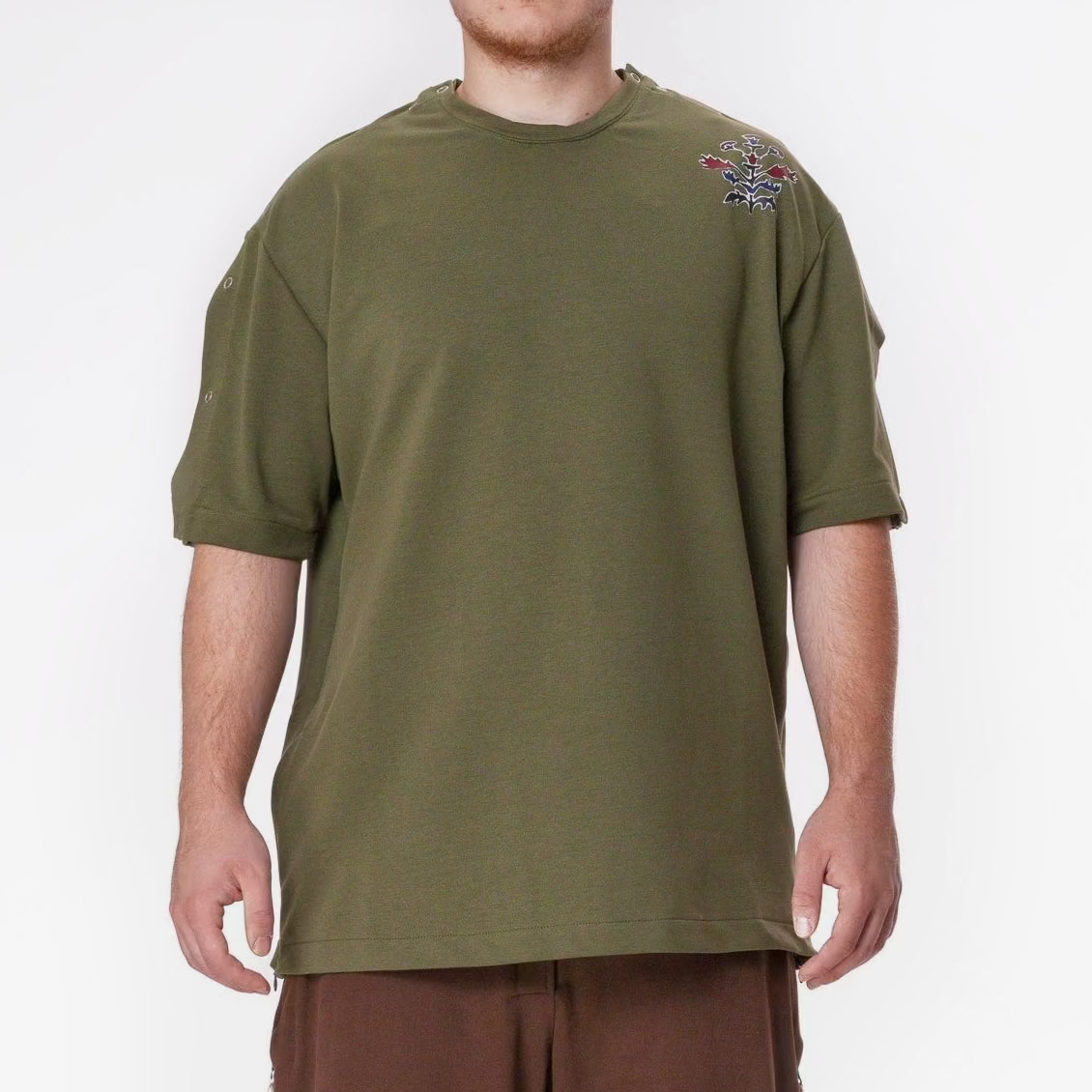 Person wearing an olive green t-shirt and brown pants on a white background