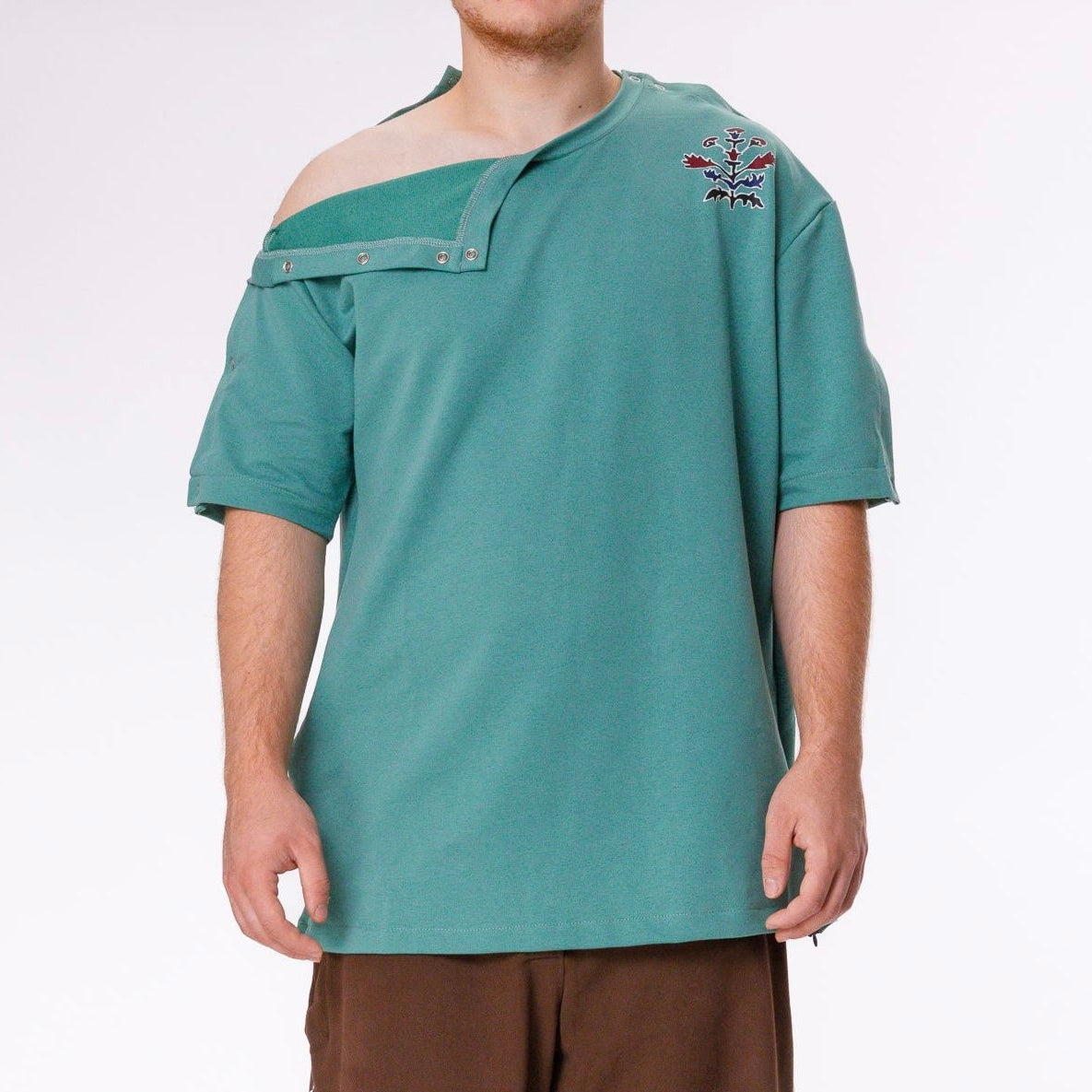 Person wearing a green off-shoulder top and brown pants on a white background